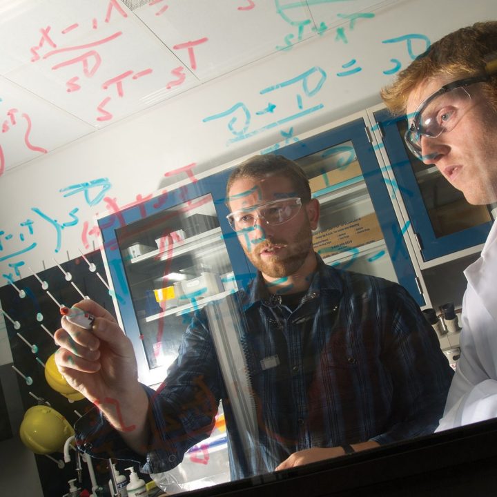 Two men in research setting collaborate using glass markerboard